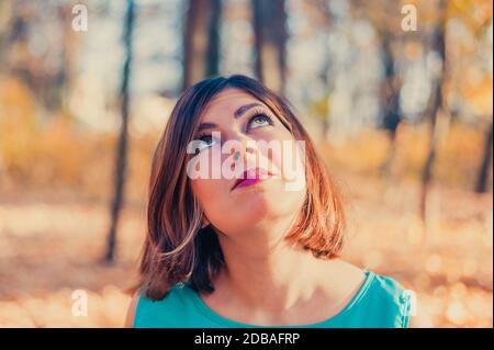 une jolie jeune fille à poil rouge en vêtements bleus regarde dans le parc d'automne Banque D'Images