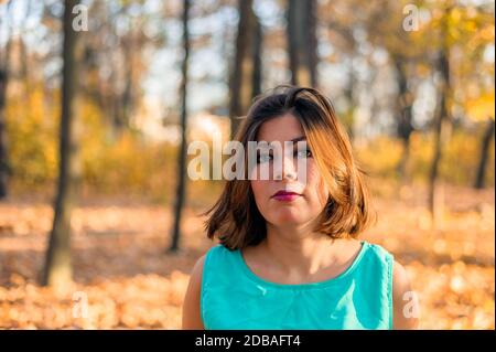 jolie fille à poil sombre avec maquillage et lèvres rouges en vêtements bleus dans la forêt jaune d'automne Banque D'Images