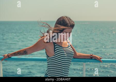 Portrait d'une belle jeune femme aux cheveux noirs avec un tatouage sur son bras dans un T-shirt rayé serré sur un fond bleu de mer Banque D'Images