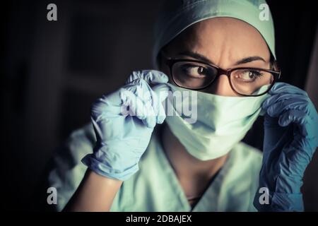 Gros plan d'un médecin femme ajustant son masque chirurgical et ses lunettes, en lumière naturelle. Banque D'Images