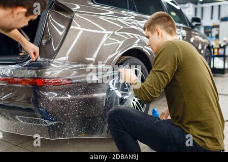 Des spécialistes appliquent un film de protection de voiture sur le pare-chocs arrière. Installation d'un revêtement qui protège la peinture de l'automobile des rayures. Véhicule neuf en g Banque D'Images