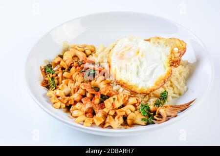 Sauté de calmars épicé avec des feuilles de basilic et le piment, oeuf au plat, servi avec du riz brun. Sex et plat épicé. Banque D'Images