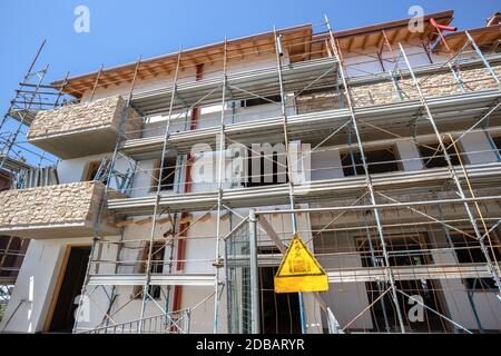 Échafaudage près d'une maison en construction pour les travaux de plâtre externe. Immeuble d'appartements moderne en ville avec balcons en pierre. Banque D'Images