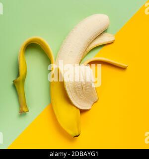 Banane à moitié pelée sur fond vert et jaune Banque D'Images