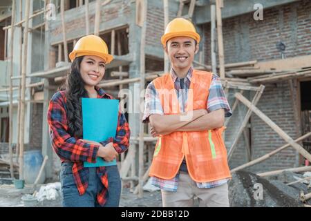 Des ouvriers du bâtiment asiatiques souriant des hommes et des femmes à la caméra port de gilets et de casques de sécurité dans des bâtiments non finis Banque D'Images