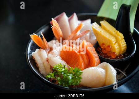 Le set de sashimi est magnifiquement agencé dans une plaque noire décorée de feuilles vertes. Buffet de cuisine japonaise. Choix du chef : saumon, hamachi, pétoncle Banque D'Images