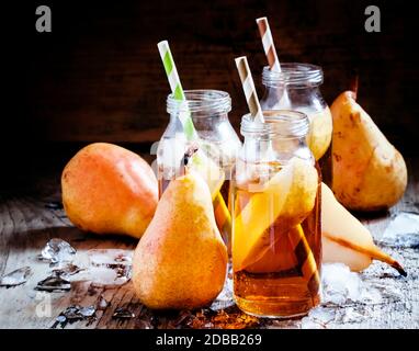 Jus de poire clarifié avec de la glace et des tranches de fruits dans des bouteilles de verre avec des pailles sur un fond en bois foncé, foyer sélectif Banque D'Images