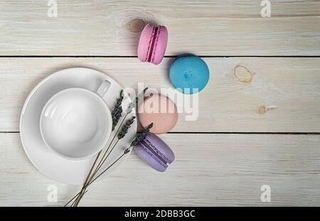 Des macarons multicolores près d'une tasse de café blanc et d'une vue sur le sommet de la lavande sur une table en bois Banque D'Images
