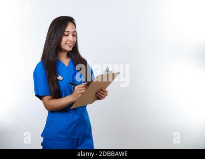Une jolie infirmière en gommage bleu écrit des notes sur son plan de travail. Banque D'Images