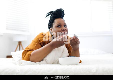 Femme couché sur le lit, mangeant des myrtilles et regardant la télévision Banque D'Images