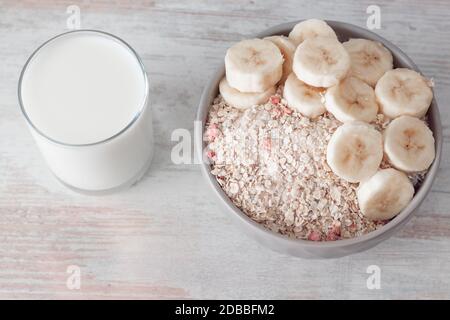 Bol de flocons d'avoine secs avec baies sèches et tranches de banane fraîche et verre de lait sur table en bois. Vue de dessus avec espace de copie. Simple santé br Banque D'Images