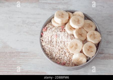 Bol de flocons d'avoine secs avec baies sèches et tranches de banane fraîche sur une table en bois. Vue de dessus avec espace de copie. Petit déjeuner sain et simple. Banque D'Images