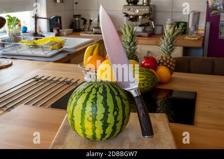 Vue rapprochée sur le melon d'eau douce et un couteau de cuisine de damas debout sur une île de cuisine dans une cuisine domestique avec d'autres variétés de fruits dans le TH Banque D'Images