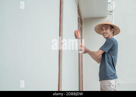 Un peintre avec un chapeau peint à l'aide d'une peinture rouleau sur une construction de bâtiment Banque D'Images