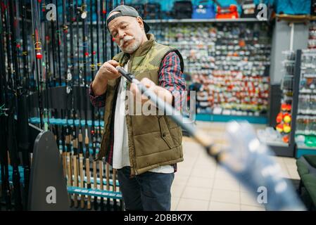 Un pêcheur à la ligne choisit la canne dans un magasin de pêche. Équipement et outils pour la chasse et la capture de poissons, choix d'accessoires en vitrine en magasin, gains et télé Banque D'Images