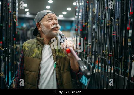 Le pêcheur à la ligne mâle tient la canne dans la boutique de pêche. Équipement et outils pour la chasse et la capture de poissons, choix d'accessoires sur la vitrine en magasin, les gains et le télescope Banque D'Images