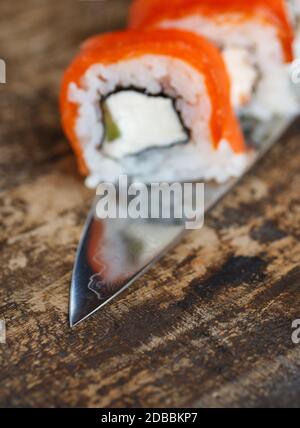 Des petits pains à sushi avec légumes, fromage et saumon sont disposés sur une lame de couteau. Sur un tableau noir rustique Banque D'Images