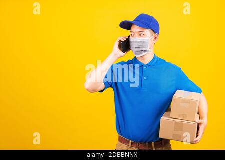 Homme de jeune living asiatique t-shirt et casquette uniforme porter masque de protection utiliser le téléphone mobile intelligent appel au client sous coronavirus ou COVI Banque D'Images
