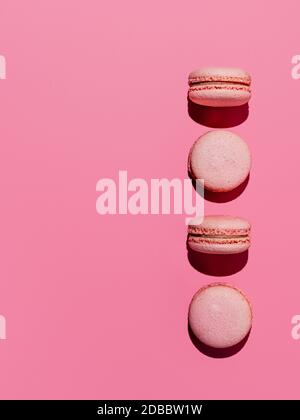 Macarons roses avec espace de copie. Rangée de macarons ou macarons français parfaits sur fond rose. Vue de dessus ou plat. Lumière dure Banque D'Images