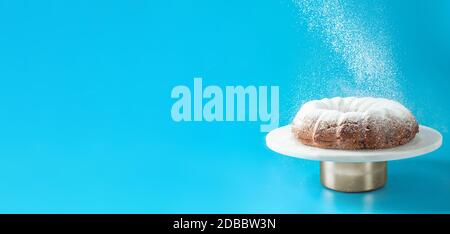 Sucre glace tombant de gâteau de petit pain frais fait maison. Le sucre en poudre tombe sur le gâteau frais sur fond bleu. Copier l'espace pour le texte. Idées et recettes Banque D'Images