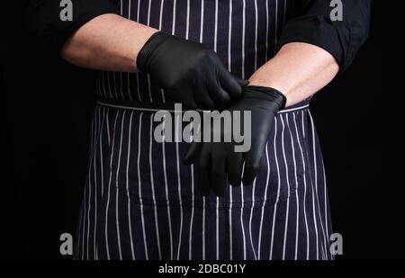 chef homme en uniforme noir et tablier rayé robes noir latex gants, faible clé Banque D'Images