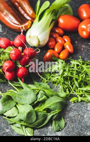 Différents légumes. Arugula, radis, épinards, poivrons rouges, tomates et pak choi sur la table de cuisine. Banque D'Images