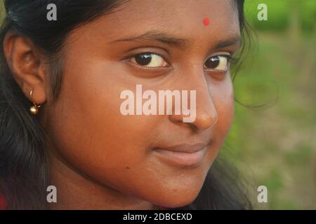 Gros plan d'une adolescente bengali indienne souriante avec de longs poils foncés portant des boucles d'oreilles de couleur dorée avec un bindi rouge sur son front. Banque D'Images