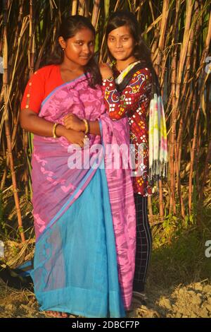 Deux belles adolescentes bengali indiennes portant sari et salwar kameez souriant et posant devant une canne à sucre plantée champ agricole Banque D'Images