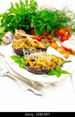 Aubergine farcie avec poitrine fumée, tomates, oignons, carottes à l'ail, fromage et herbes dans une plaque ovale sur une serviette en toile de fond de bois clair Banque D'Images