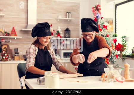 Grand-mère en tablier pendant le jour de noël pâtisserie faisant le désert avec l'enfant. Joyeux joyeux joyeux adolescente aidant la femme âgée à préparer des biscuits sucrés pour célébrer les vacances d'hiver. Banque D'Images