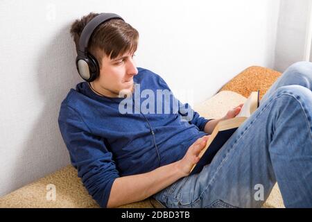 Un jeune homme dans un casque lit un livre à la maison Banque D'Images
