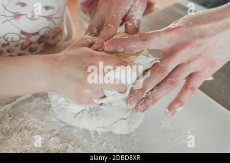 Les mains de la mère et de la fille pétrissent la pâte pour la pizza et le pain. S'amuser ensemble dans la cuisine. Gros plan. Banque D'Images