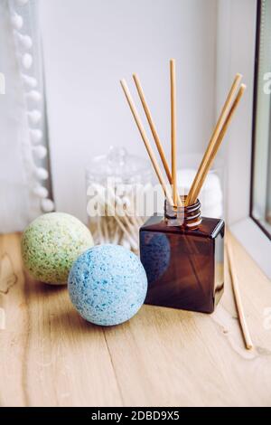 Salle de bains en bois naturel, rebord de fenêtre avec diffuseur de liquide, bouteille avec bâtons de bois, lumière naturelle provenant de la fenêtre. Bombes de bain apaisantes bleues et vertes. Banque D'Images