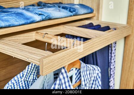 Intérieur de la garde-robe en bois avec porte-vêtements coulissant pour les coathangers. garde-robe moderne avec des vêtements suspendus sur des porte-vêtements coulissants et pliés sur le Banque D'Images