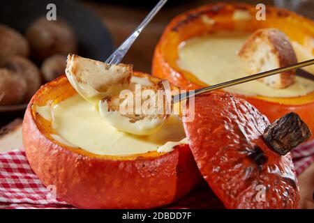 Fondue suisse traditionnelle avec fromage de raclette fondu servi dans une citrouille rôtie creuse avec baguette grillée pour la trempage, en gros plan Banque D'Images