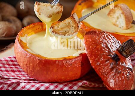 Une délicieuse fondue au fromage servie dans une croûte de citrouille orange colorée en automne, en gros plan avec des fourchettes qui trempent de la baguette grillée Banque D'Images