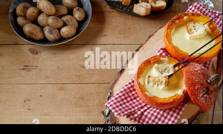 Service de fondue au fromage suisse traditionnelle dans des citrouilles d'automne rôties, servies avec des pommes de terre de bébé cuites et des baguettes grillées pour y plonger Banque D'Images