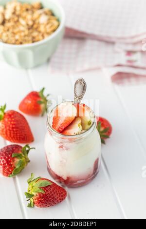 Yaourt blanc fruité dans un pot et fraises sur table blanche. Banque D'Images