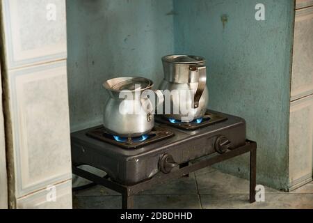 Chauffer du lait et de l'eau pour faire du café sur un vieux poêle en métal dans des cruches en métal Banque D'Images