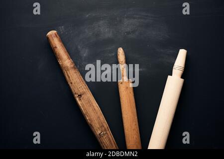 trois types de goupilles à roulettes en bois pour faire rouler la pâte sur fond noir, ustensiles neufs et très anciens, vue de dessus Banque D'Images