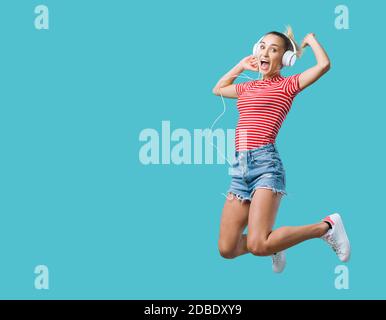 Jeune femme joyeuse portant des écouteurs et écoutant de la musique, elle saute et se sent excitée Banque D'Images