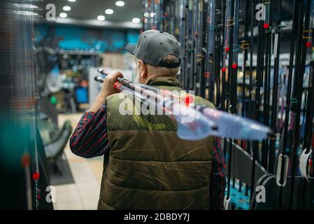 Le pêcheur à la ligne mâle tient la tige avec la bobine dans la boutique de pêche. Équipement et outils pour la pêche et la chasse au poisson, choix d'accessoires sur la vitrine en magasin, gains a Banque D'Images