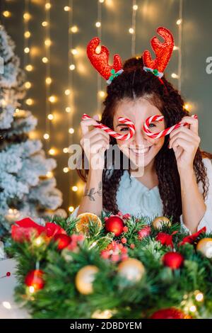 Belle femme souriante de cheveux afro portant blanc pull dans Décoration de Noël avec lumières sur fond Banque D'Images