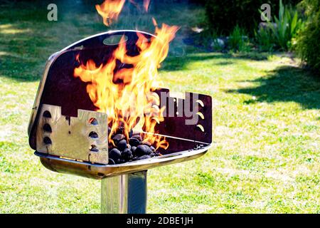 Gros plan du moment gelé des flammes flamboyantes dans un grill au charbon de bois avec fond d'herbe verte d'un jardin. Prépearing d'une fête barbecue à a s. Banque D'Images