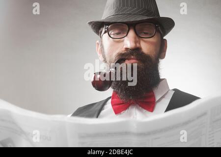 L'élégant vieil homme d'âge moyen à barbe avec pipe à tabac lit le journal. Banque D'Images