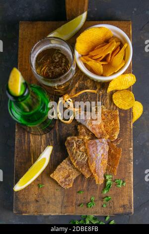 Morue séchée au poivre avec bière, citron et chips de pomme de terre sur un panneau en bois sombre. En-cas sur le poisson avec de la bière. Gros plan. Banque D'Images