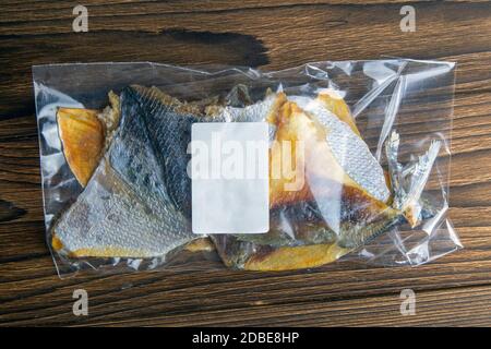 Dorade séchée en forme de papillon dans un emballage transparent avec une étiquette blanche apéritif à la bière sur fond de bois. Snack Fish à la bière. Gros plan. Banque D'Images