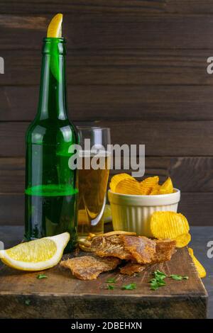 Morue séchée au poivre avec bière, citron et chips de pomme de terre sur un panneau en bois sombre. En-cas sur le poisson avec de la bière. Gros plan. Banque D'Images