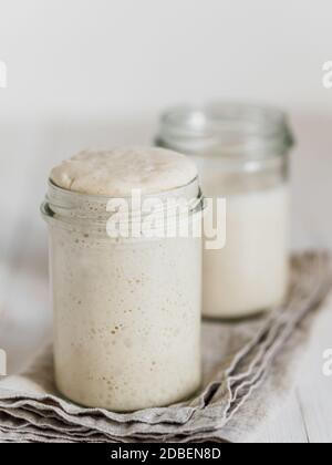 Deux pots en verre avec des démarreurs de levain de blé dans différents niveaux d'hydratation. Starter 100 % d'hydratation au premier plan et Starter avec hy plus élevé Banque D'Images