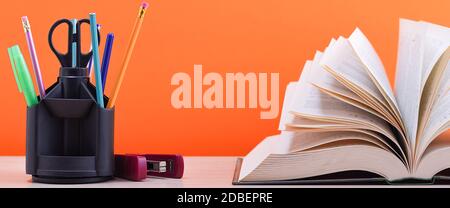 Un livre et un support avec des stylos, des crayons et des ciseaux sur une table en bois clair. Le livre est ouvert, les feuilles de la page sont bronzées, un dos brun orange Banque D'Images